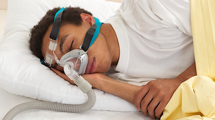 Young sleep apnea patient sleeping on side with CPAP mask fitted.