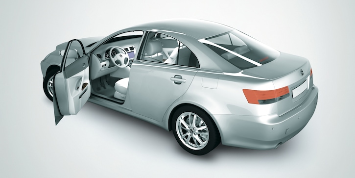 A silver saloon car with an open front left door taken from a rear side angle  against a gradient grey background.