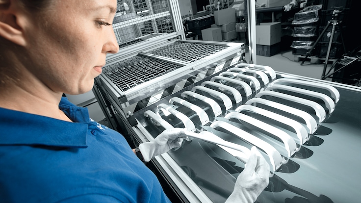 Worker in white gloves inspecting one of twenty moulded fridge handles coming on a production line.
