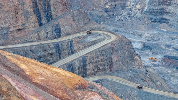 Aerial perspective of mining trucks meandering along a winding road through an open pit mine.