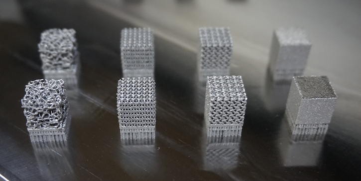 A collection of eight metallic blocks showing thin, complex lattice structures sitting on a surface. 
