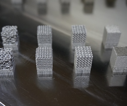 A collection of eight metallic blocks showing thin, complex lattice structures sitting on a surface. 