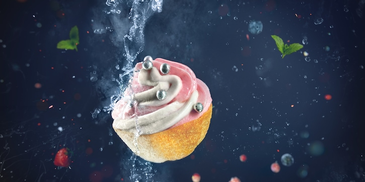 An artistic photograph of a cupcake with colorful sprinkles being partly frozen with liquid nitrogen on a dark background