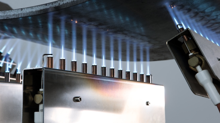 Close up of three  LINDOFLAMM special burners each showing a row of twelve extremely focused white flames heating a curved metal part.