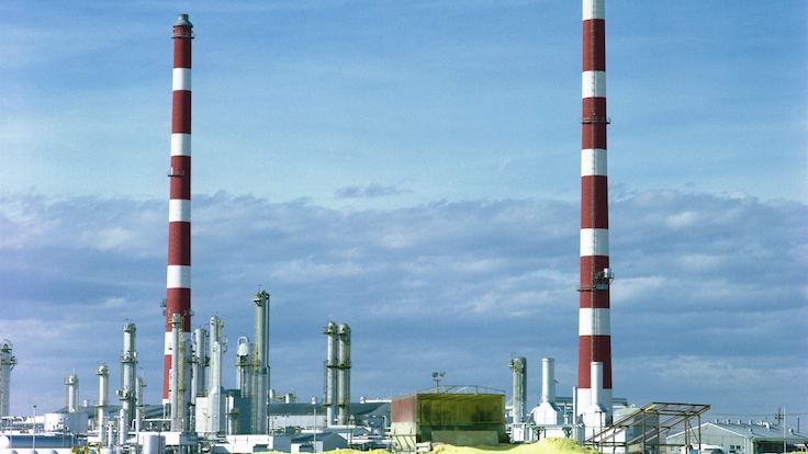 A sulfur recovery site with yellow piles of sulfur outside against the backdrop of emission towers